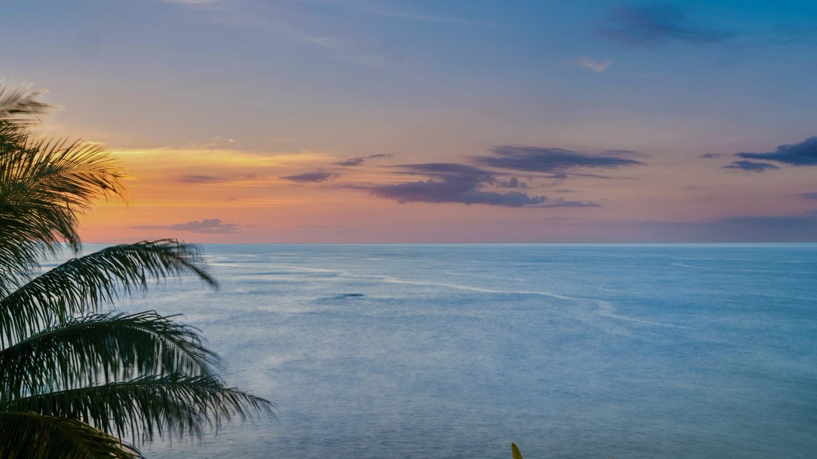 Sunset over the Pacific from the oceanfront lanai of the Wailua Bay View condo on Kauai, framed by palm trees.